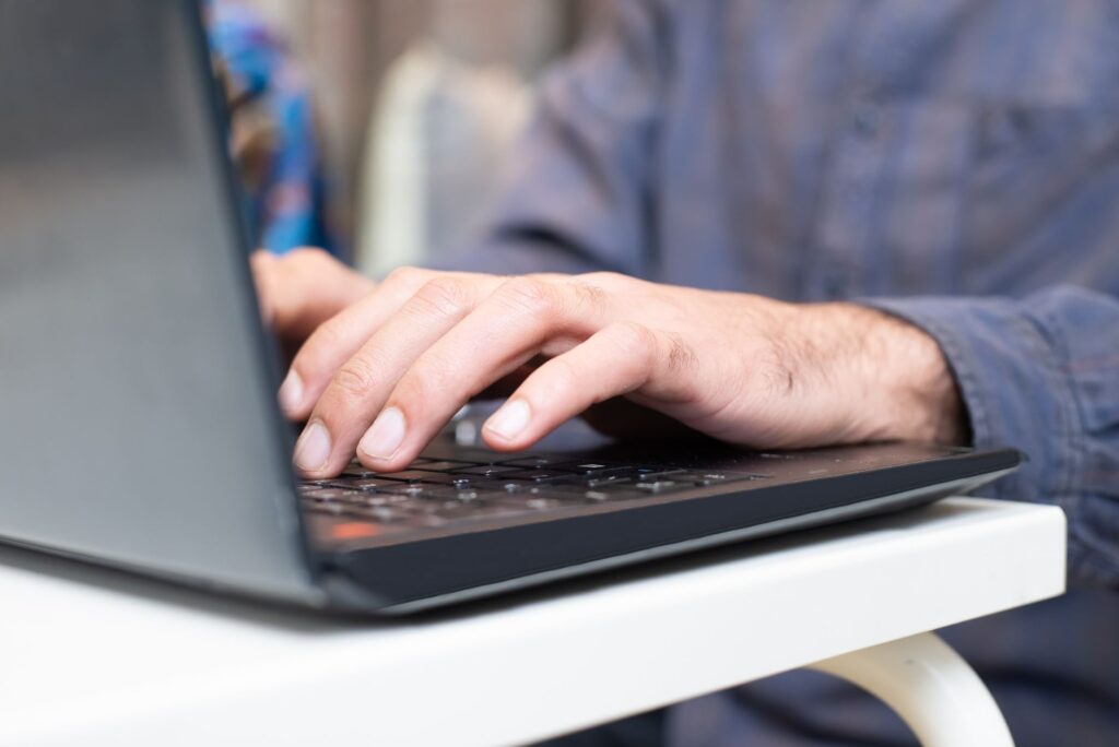 Hände tippen auf der Tastatur eines aufgeklappten Laptops