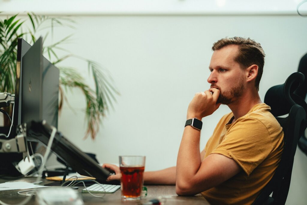 Mann sitzt nachdenklich vor seinem Monitor am Schreibtisch