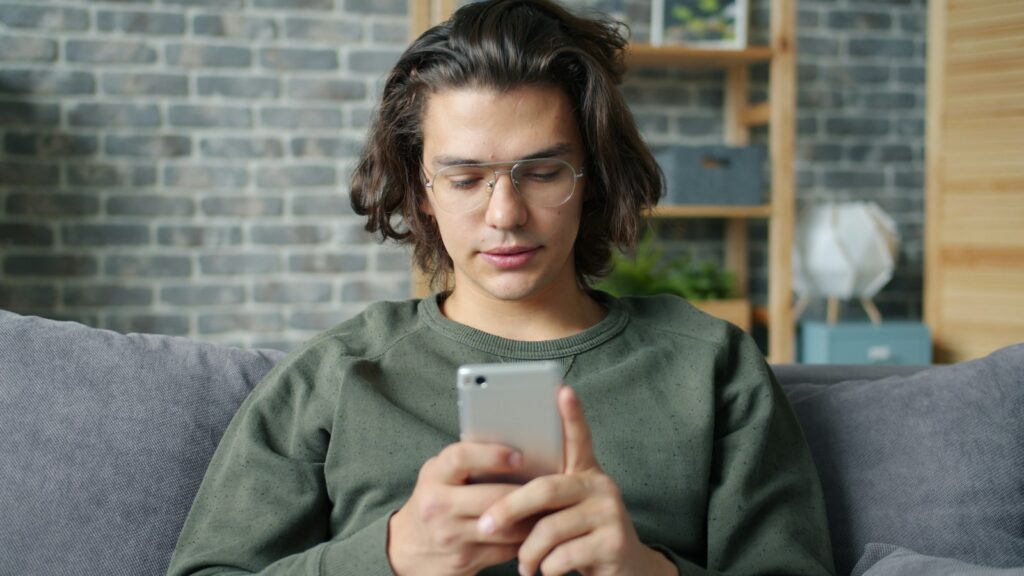 Mann sitzt auf dem Sofa und schaut auf sein Smartphone, etwa um den Stand eines Backups zu prüfen