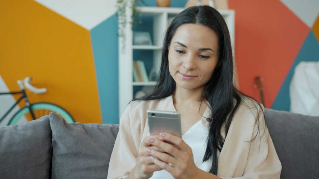 Frau sitzt auf dem Sofa und schaut auf ihr Smartphone, etwa um den iCloud-Speicher zu prüfen