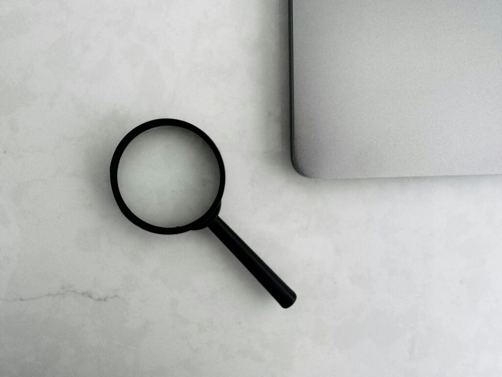 Lupe neben einem Laptop als Symbol für das Prüfen von Online-Quellen