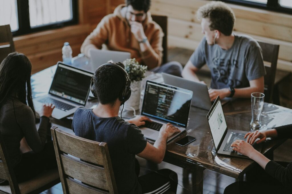 Team arbeitet an Laptops an einem Holztisch, auf einem Bildschirm ist Programmcode zu sehen