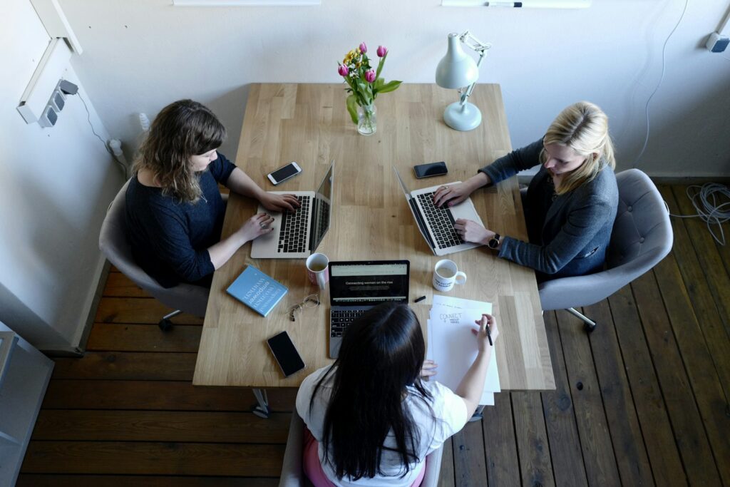Drei Kolleginnen arbeiten an einem Holztisch gemeinsam an ihren Laptops