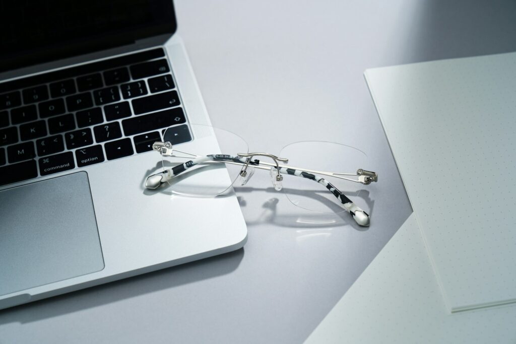Brille liegt auf einem aufgeklappten Laptop auf einem hellen Schreibtisch