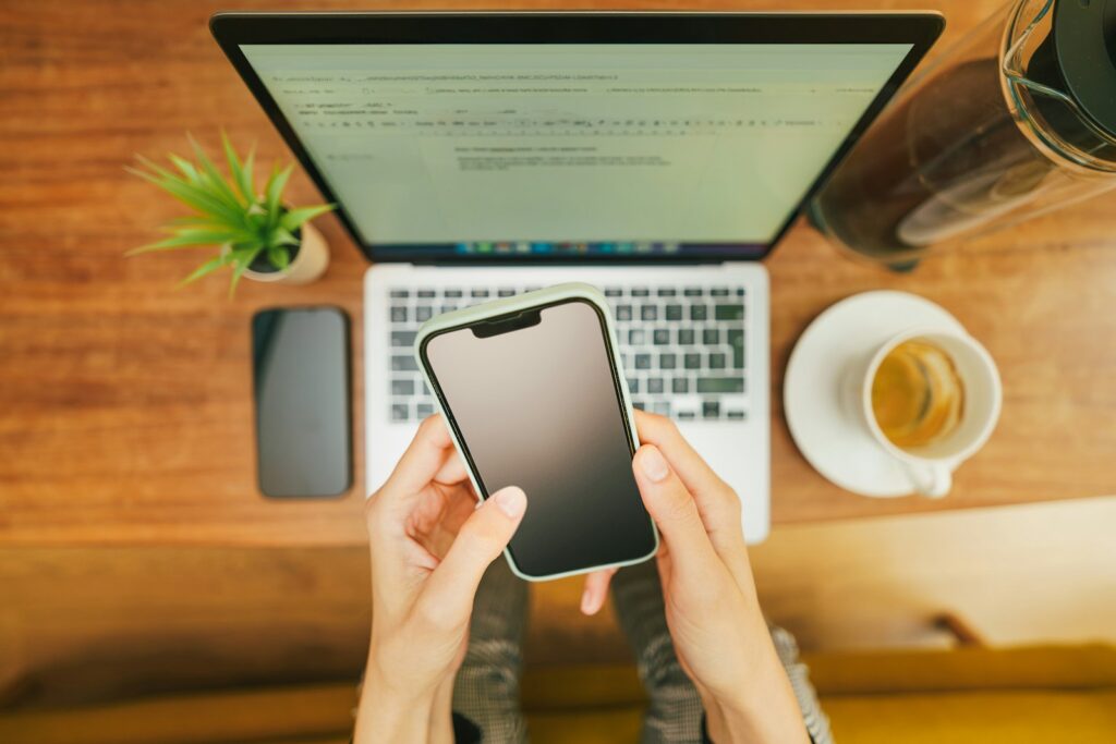 Person hält ein Smartphone vor einem Laptop auf dem Schreibtisch, Symbolbild für Chat-Backups